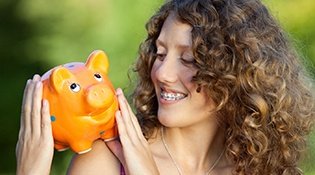 Woman with braces smiling at piggy bank on shoulder