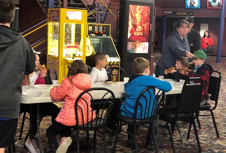 Kids at tables eating pizza during community Involvement movie theater event