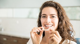 a woman smiling while holding her clear aligners
