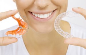 A woman holding two types of orthodontic retainers.