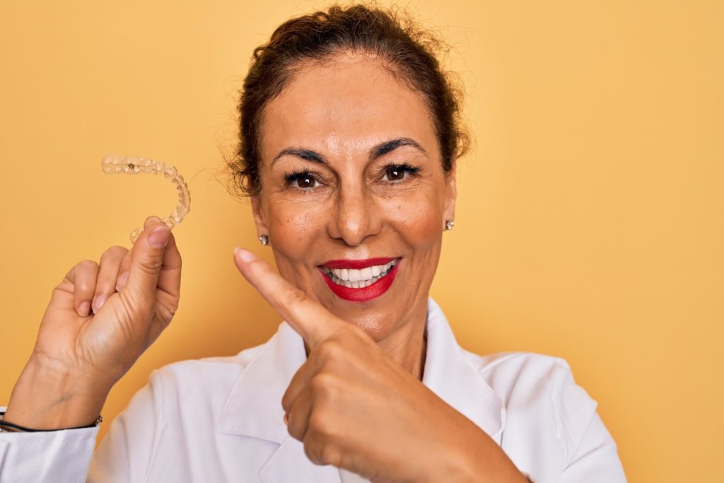 Mature woman smiling while holding clear aligner